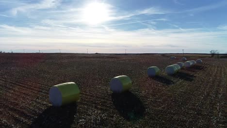 Toma-Aérea-De-Drones-De-Barrido-De-Una-Granja-De-Algodón-Del-Medio-Oeste-Con-Pacas-Frescas-De-Algodón-Cosechado-Envuelto-En-Material-Amarillo-Brillante-Contra-Un-Cielo-Azul-Abierto