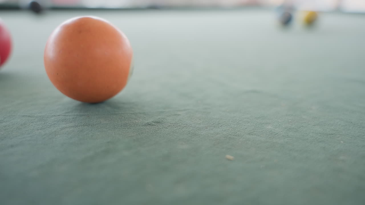 Primo piano di una palla da biliardo arancione sul panno, un polpastrello spinge la palla, rotolamento lento su un tavolo verde testurizzato, profondità di campo ridotta, luce naturale soffusa, atmosfera di pratica intima che evidenzia cuciture e venature.