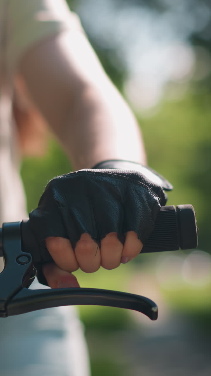 primer plano del manillar de la bicicleta individual con la mano con guante, acelerando y sosteniendo el freno con la luz solar reflejada en la mano, el fondo está suavemente borroso con vegetación natural