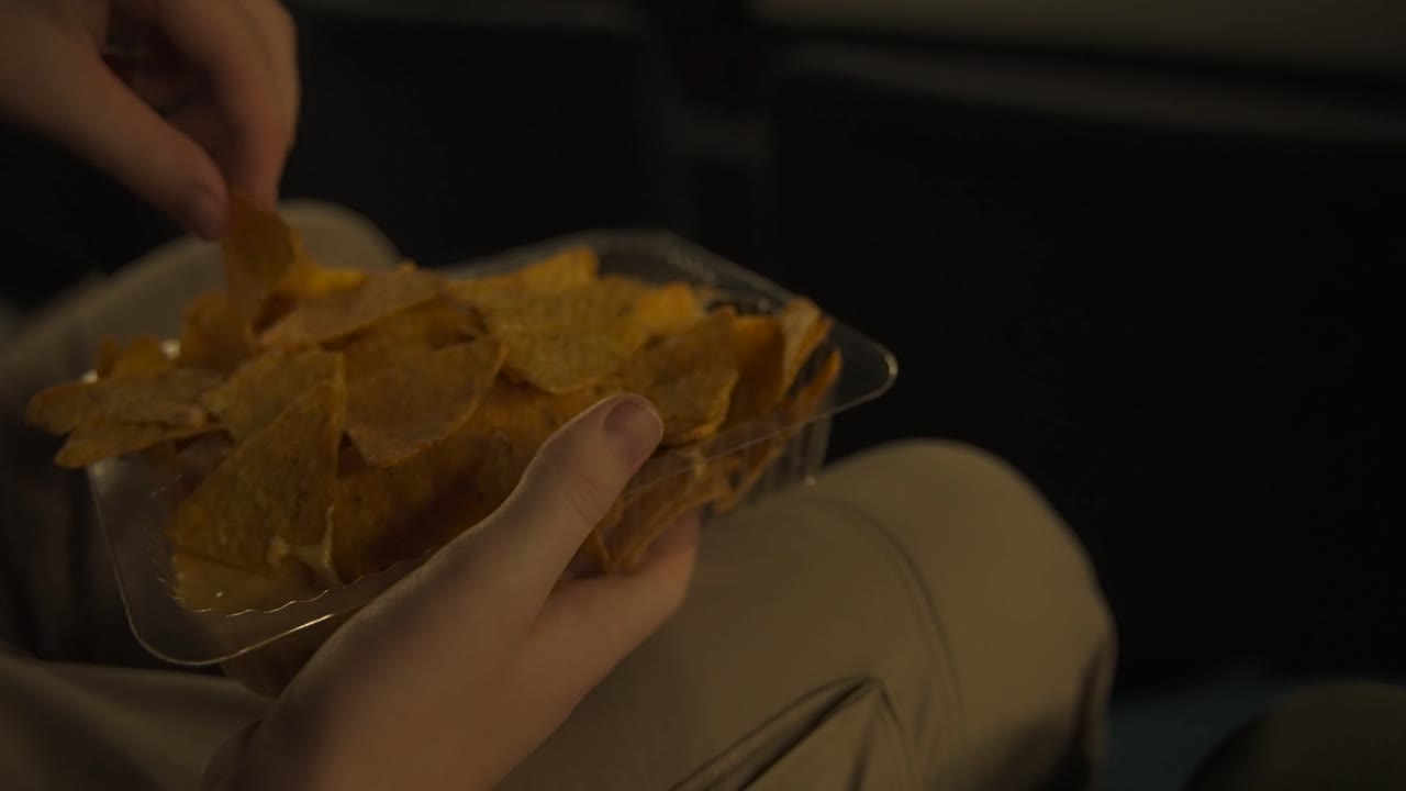 Mangiare nachos al cinema davanti a uno schermo bianco, primo piano lento.
