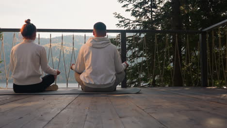 couple meditating on a deck overlooking a lake in the mountains