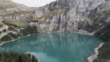 Crystal-clear-turquoise-lake-surrounded-by-majestic-mountains-and-lush-greenery,-aerial-view