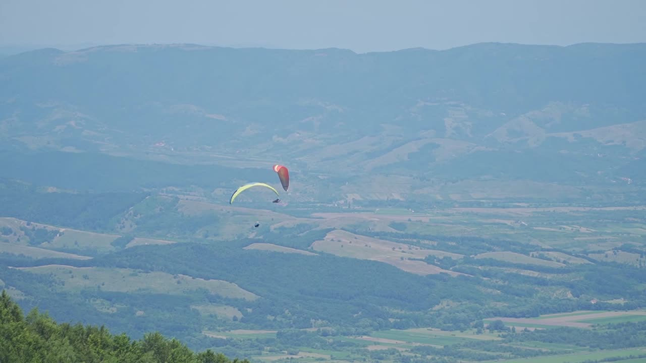 An adrenaline-filled moment in the sky—two paragliders navigate close encounters and smooth turns above a stunning landscape.