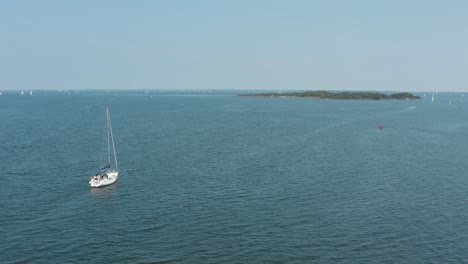 Filmische-Drohne---Luftaufnahme-Eines-Bootes,-Das-An-Einem-Sonnigen-Tag-Auf-Dem-Welligen-Ozean-Segelt,-Mit-Einer-Insel-Und-Anderen-Surfern-Im-Hintergrund,-30p