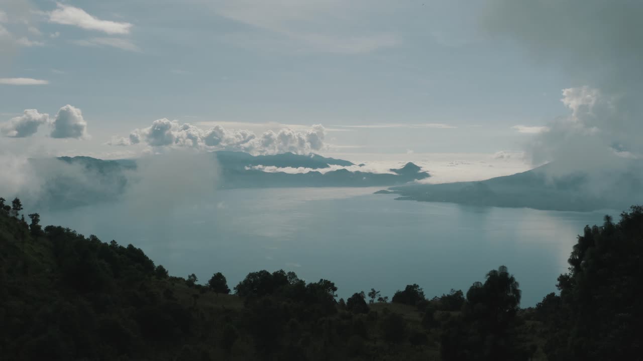 vista aérea de drones, volando sobre árboles de silueta, revelando el hermoso lago azul atitlan, guatemala