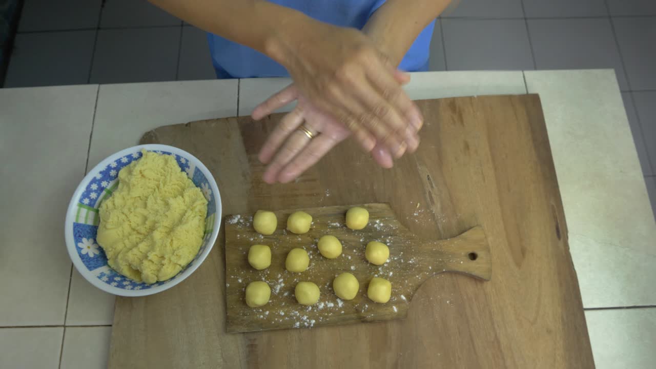 haciendo galletas manos de la mujer amasar y rodar bolas redondas de pan de la masa en la tabla de corte base de madera en la cocina