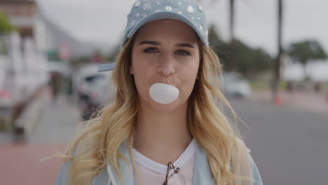 Retrato-De-Una-Linda-Joven-Rubia-Soplando-Chicle-Mirando-La-Cámara-Disfrutando-De-Unas-Vacaciones-Urbanas-Frente-A-La-Playa-En-Una-Soleada-Calle-Urbana