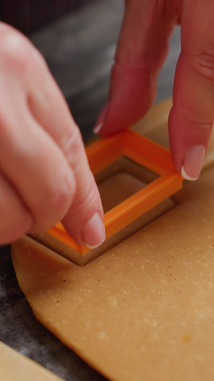 close-up de mulher pressionando cortador de biscoitos laranja em massa, criando forma precisa, mãos cuidadosamente manicured, preparação de panificação, guias de madeira para espessura uniforme, bancada texturizada