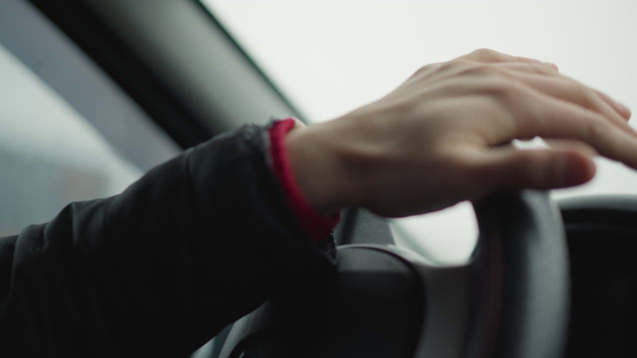 Close up hand view of driver turning steering wheel in smooth professional motion with blurred tree lined road visible through window reflection, emphasis on precise hand grip and wheel texture