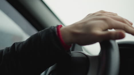 close up hand view of driver turning steering wheel in smooth professional motion with blurred tree lined road visible through window reflection, emphasis on precise hand grip and wheel texture