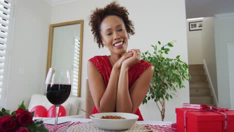 Happy-mixed-race-woman-on-a-valentines-date-video-call,-drinking-wine