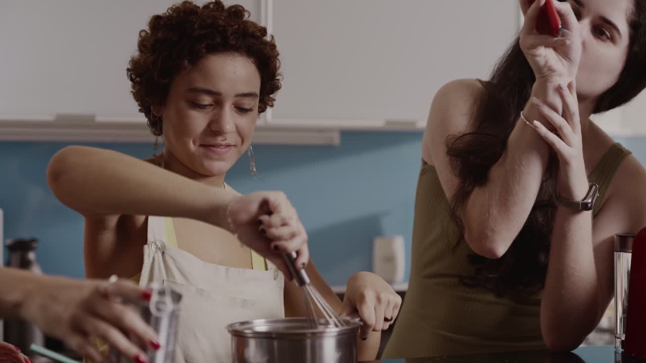 Two Women Cooking Together in a Kitchen, Consulting a Smartphone
