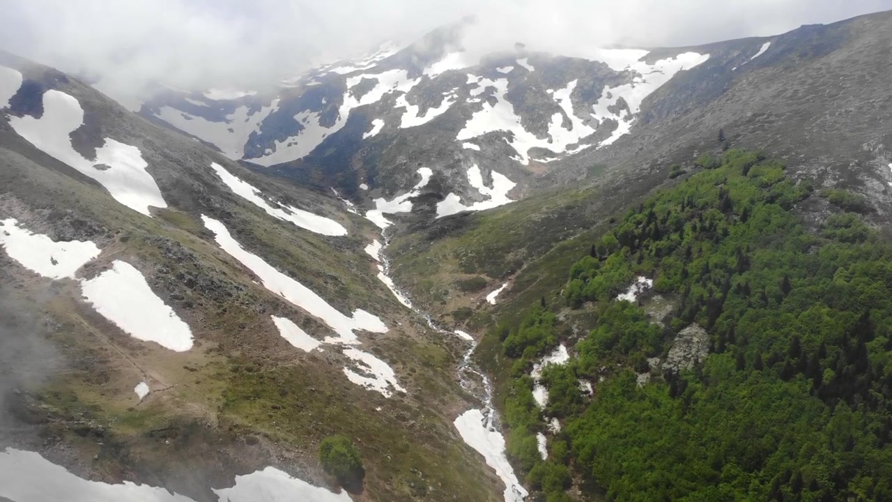 Vista aerea di una valle montuosa innevata con ruscello e foresta.
