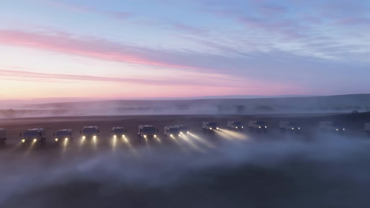 Scatto panoramico dall'alto che mostra una fitta nebbia che si accumula su un paesaggio pianeggiante e un bordo industriale, mentre una fila di luci bianche brillanti taglia la nebbia vicino alla parte inferiore.