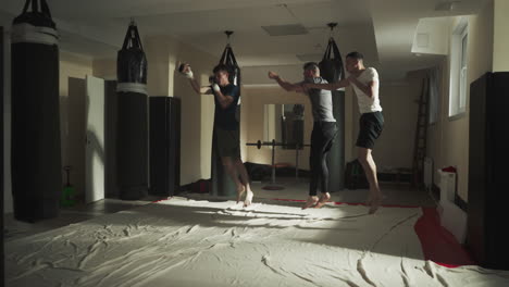 fighters jump and punch air imitating strikes training in gym. sportsmen group does physical exercises together in martial arts club slow motion. combat athlete