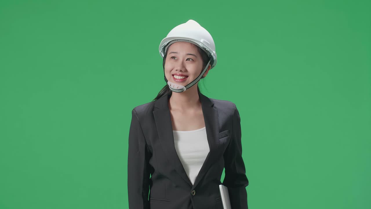 Smiling Asian Female Engineer With Laptop Looking Around And Shaking Her Head In The Green Screen Studio