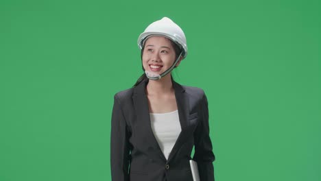 smiling asian female engineer with laptop looking around and shaking her head in the green screen studio