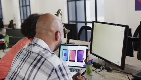 Two-happy-diverse-designers-in-discussion-at-computer-with-copy-space-in-casual-office,-slow-motion