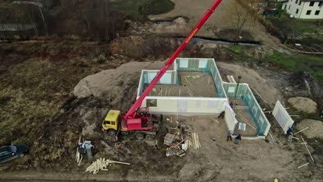 aerial shot of a house under construction with crane and workers surrounded by nature and trees