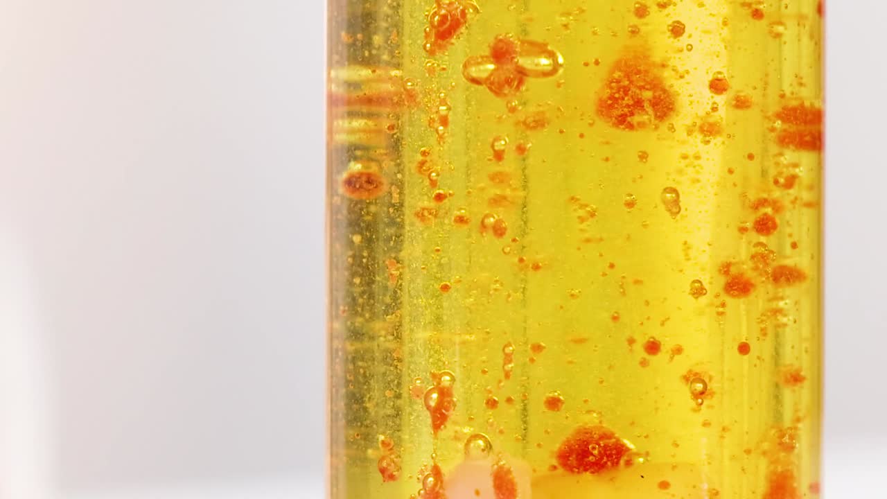 Visão macro de gotas e bolhas vermelhas se movendo através de um fluido amarelo dentro de um tubo de vidro