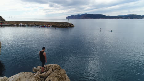 Toma-De-Drone-De-Un-Hombre-Que-Se-Queda-En-Un-Acantilado-En-Mallorca-Y-Mira-Hacia-El-Horizonte,-4k-Uhd