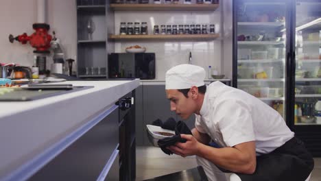 cocinero de raza mixta vestido con ropa blanca en una cocina de un restaurante, sacando comida de un horno