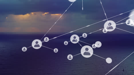 animation of network of connections with people icons over sea, sky with clouds