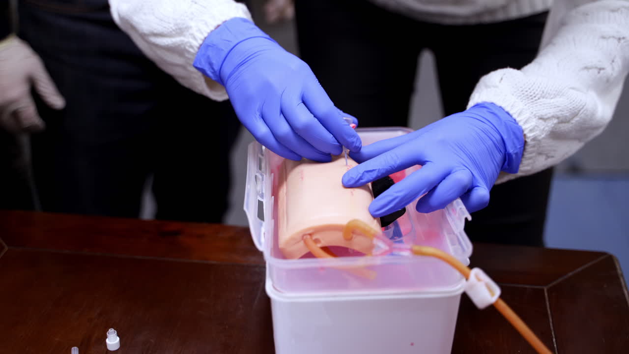 Hands in gloves doing injection on a dummy arm. Practitioner learning to prick with a syringe into a mannequin hand. Close-up.
