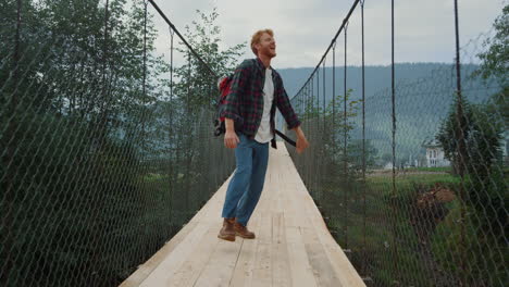 energetic man backpacking mountains on nature hike. tourist jump on river bridge