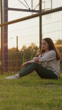 una mujer joven se sienta en el césped del estadio deportivo. los rayos de sol iluminan a una mujer contemplativa que reflexiona sobre la idea de consultar a un psicólogo para abordar los problemas.
