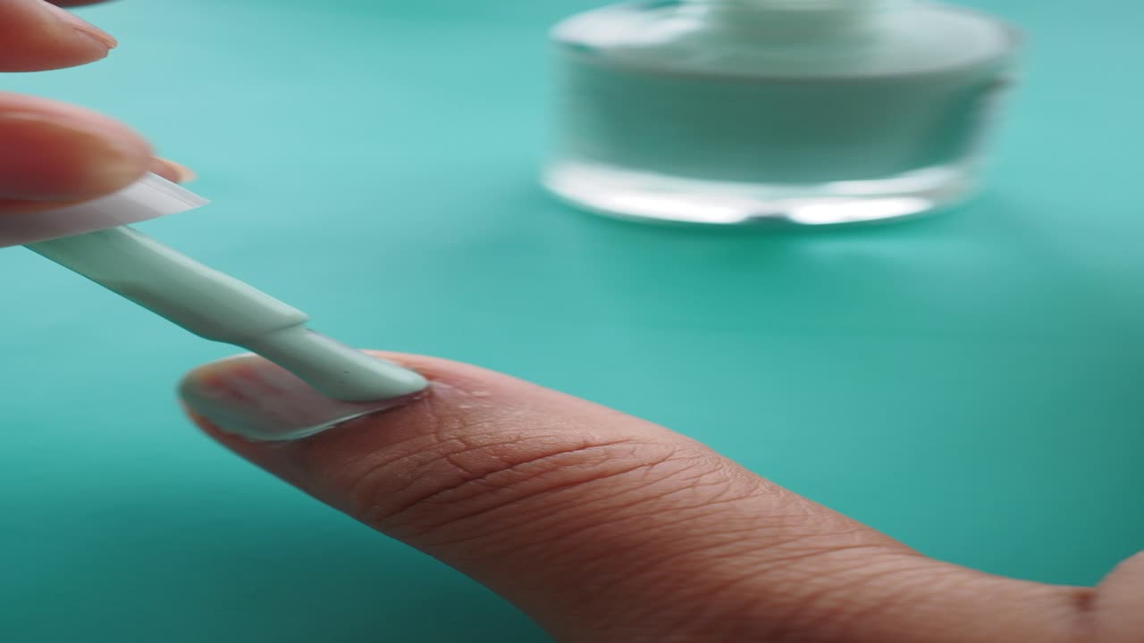 cerca de una mano aplicando esmalte de uñas verde menta
