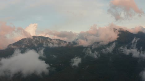 aerial drone shot of green forest covered mountains, flying through light wispy clouds at sunset, sunrise