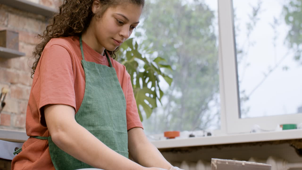 vista inferior de una empleada que modela una pieza de cerámica en una rueda de alfarero en un taller