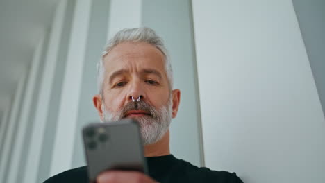 un anciano barbudo usando un teléfono móvil de primer plano. un hombre brutal y confiado con una perforación.
