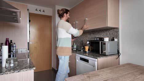 A man in a kitchen opening cabinets and using appliances