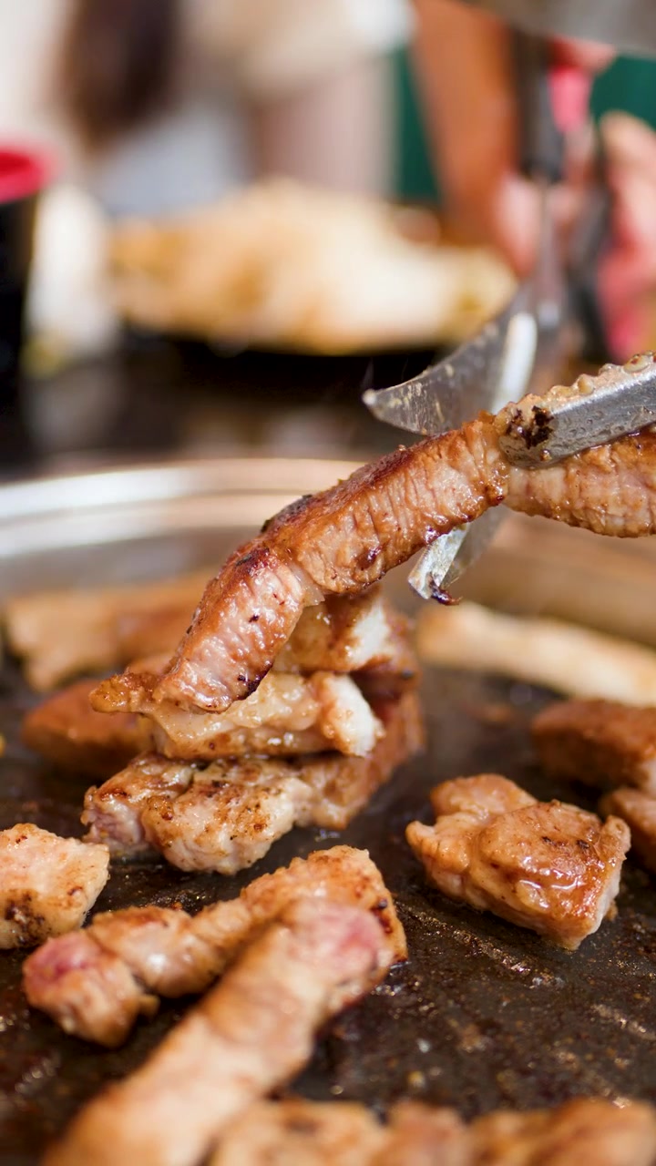 Una mano usa pinze e forbici per tagliare pancetta di maiale grigliata su una griglia coreana da barbecue da tavolo.