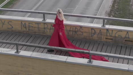 Aerial-drone-shot-of-a-model-walking-on-a-bride-with-a-beautiful-vibrant-red-dress