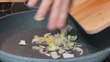 hand dropping leeks into a frying pan from a wooden cutting board