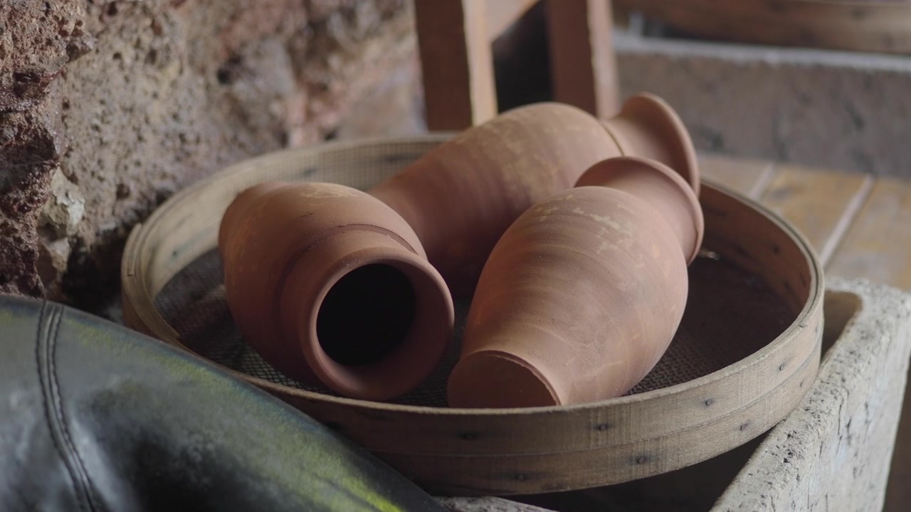 Three Handmade Clay Pottery Jars Resting in a Wooden Sieve