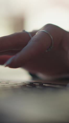 primer plano de manos con uñas pulidas, anillos delicados y dedos elegantes escribiendo en el teclado de la computadora portátil al aire libre, con un fondo suave y borroso