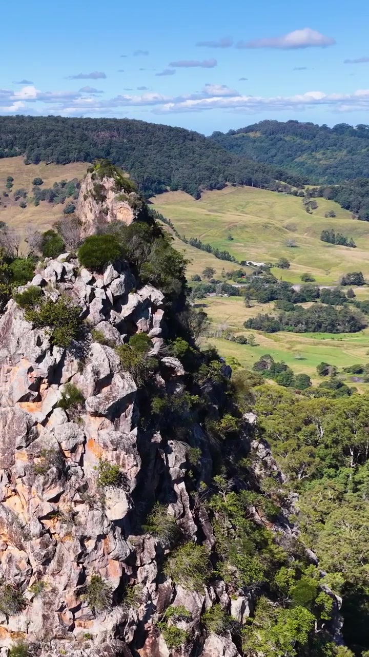 Imagens aéreas de Nimbin Rocks, exibindo vegetação exuberante e falésias rochosas sob céus azuis límpidos.