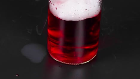 un vaso con líquido rojo reacciona con hielo seco, creando niebla y burbujas en un entorno oscuro