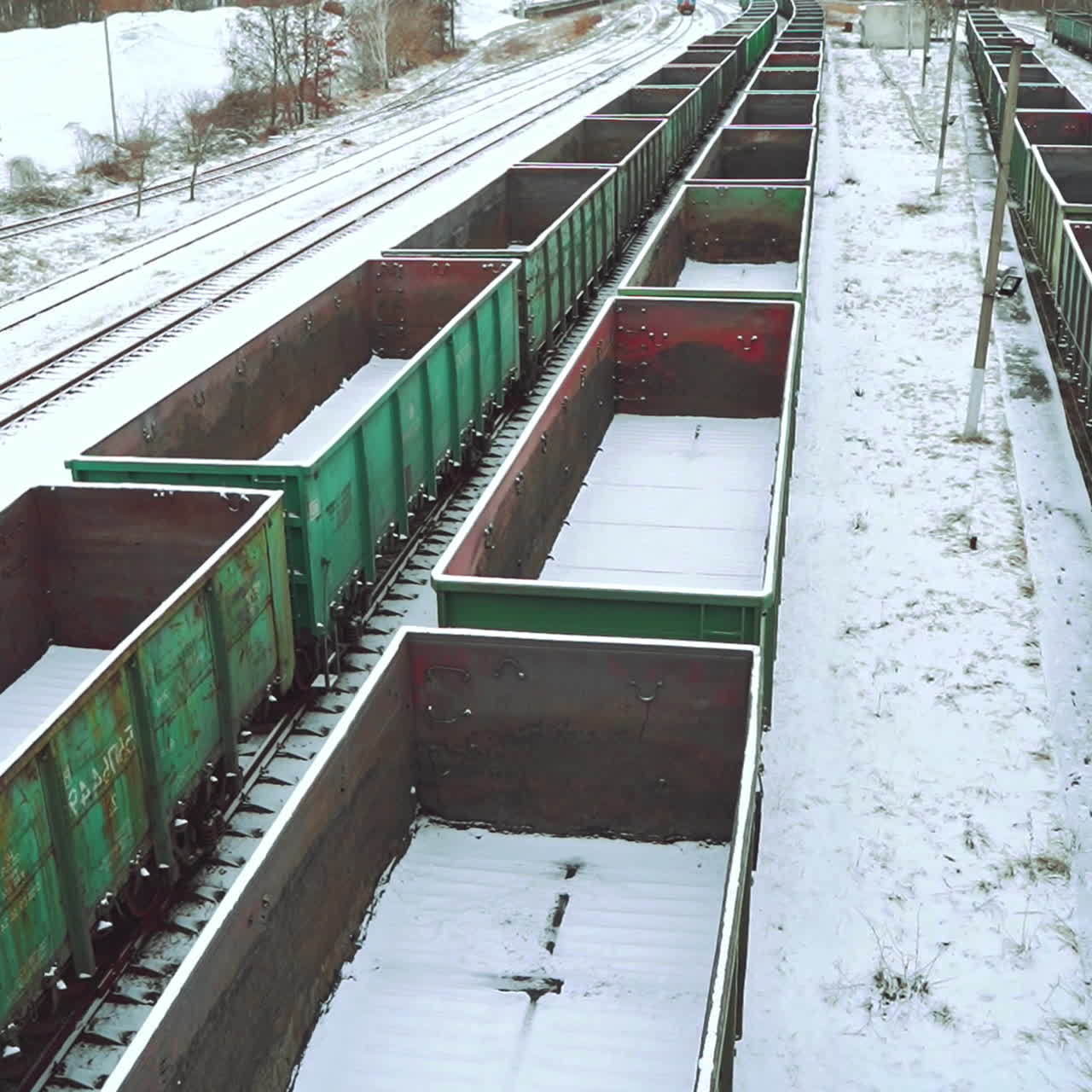 View of the rows with empty containers for the supply of goods, sprinkled with snow on the background of the railway station outside the city. Logistics.
