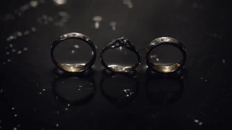 Wedding-and-engagement-rings-lying-on-dark-water-surface-shining-with-light