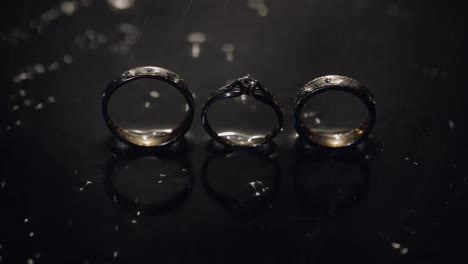 anillos de boda y compromiso en la superficie del agua oscura brillando con luz