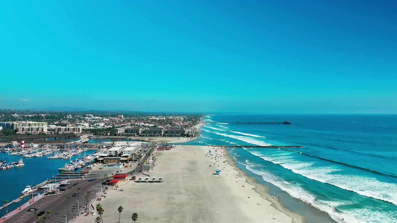 カリフォルニア州オーシャンサイドのマリーナ。太平洋上空から、ビーチ、港、ボートを望むドローンによる右パンニング映像。