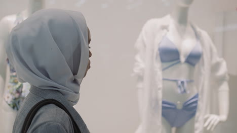 black woman with hijab looks at swimsuit in fashion store