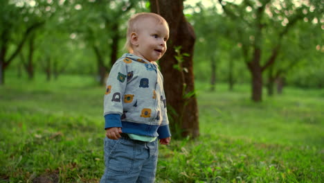 un ragazzino carino che cade a terra all'aperto. un bambino in piedi nel parco verde.
