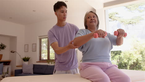 assisting senior woman with dumbbells, male physiotherapist guiding exercise session