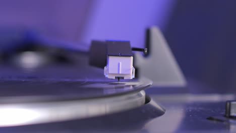 record-player-close-up-needle,-vinyl-turntable-head-that-rides-on-a-vinyl-plank,-stylus-needle,-vinyl-record-playing,-purple-blue-light,-cinematic-depth-of-field-blurry-background,-soft-focus,-retro